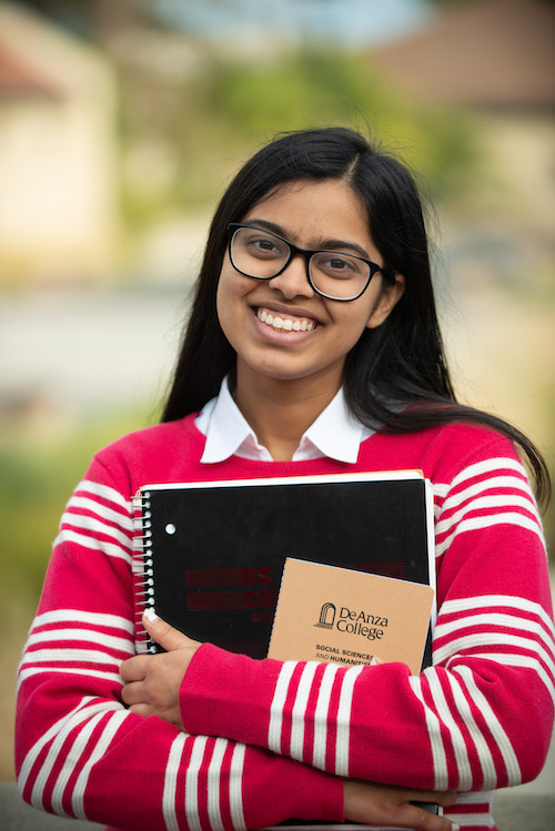young woman with glasses, holding two notebooks and smiling