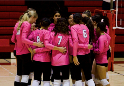 women volleyball players on court huddling with pink jerseys